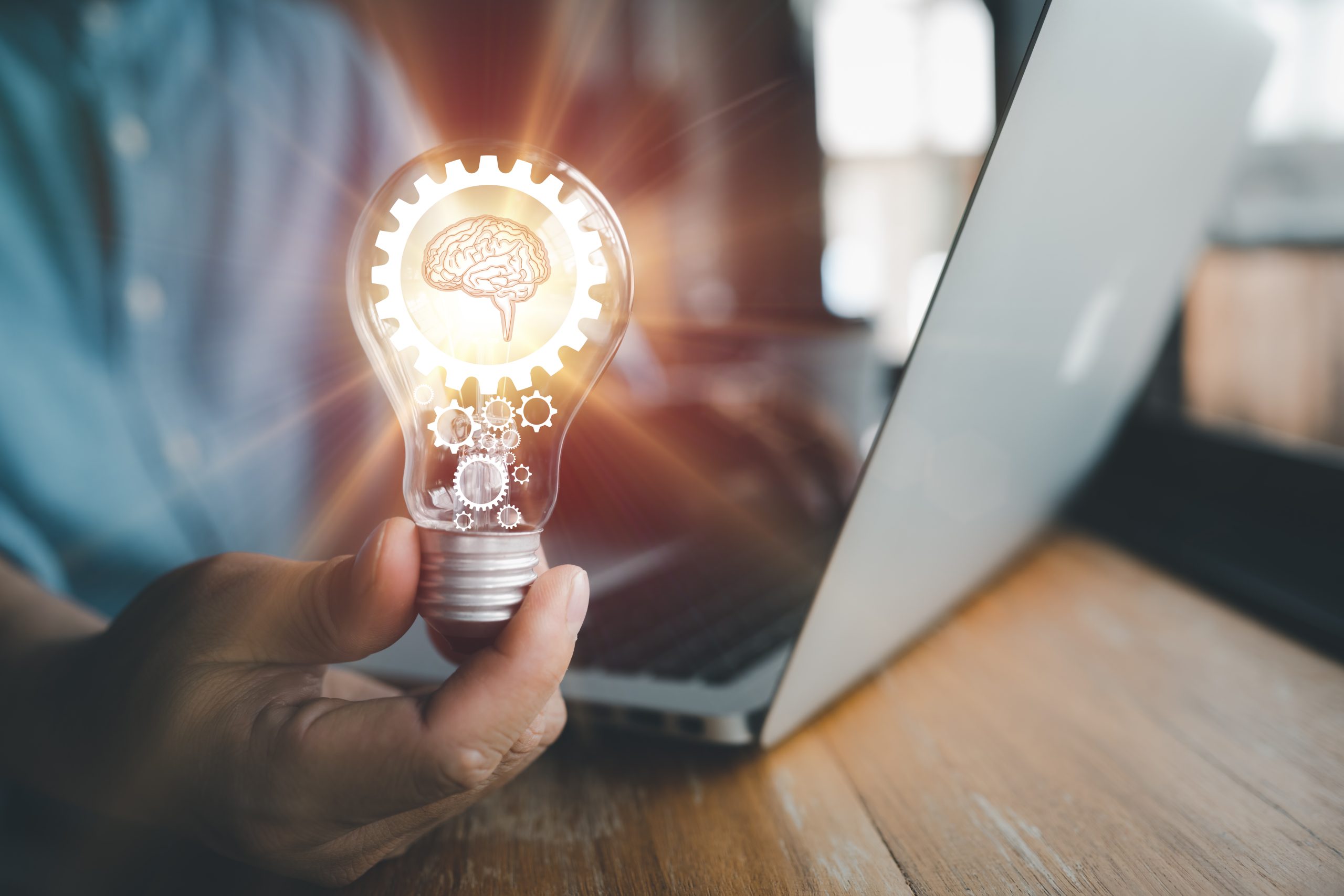 The hand of a man with a light bulb And there is a gear icon and brain in it And he is using a notebook computer. The idea of inspiration from online technology.innovation idea concept.